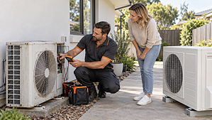 HVAC technician inspecting an older outdoor air conditioner beside a replacement unit at an Australian home.