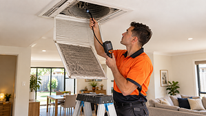 HVAC technician inspecting a dusty ceiling air duct and return air filter in an Australian home to check whether duct cleaning is needed.
